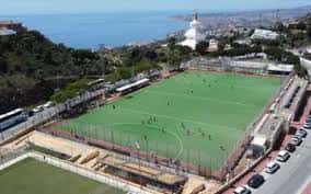 Vista aérea del complejo deportivo con campo de fútbol, alrededores costeros y mar al fondo