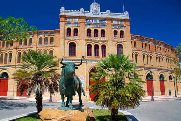 Fachada principal de la plaza de toros con la estatua del toro y palmeras