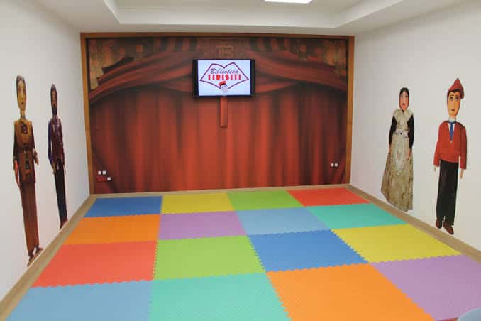 Sala de actividades con suelo de espuma multicolor y cortinas rojas decorativas