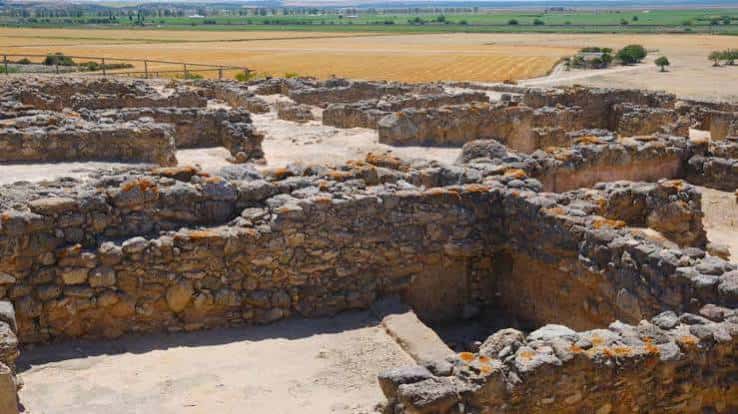 Vista panorámica de las ruinas del yacimiento arqueológico con muros de piedra y campo de fondo