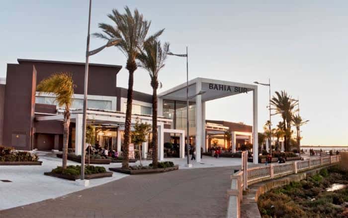 Vista exterior del Centro Comercial Bahía Sur con palmeras y acceso peatonal al atardecer
