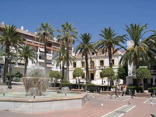Plaza con fuente, palmeras y edificios tradicionales al fondo