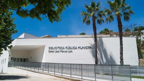 Fachada principal de la biblioteca con rampa de acceso y palmeras bajo cielo azul