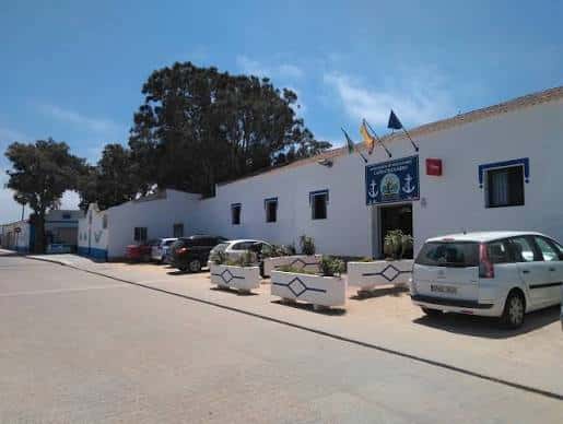 Vista exterior del edificio blanco con banderas y vehículos estacionados