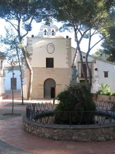 Fachada principal de la ermita con campanario y fuente decorativa en primer plano