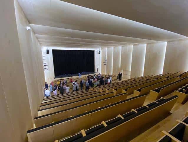Interior del auditorio durante un evento con público en las gradas y escenario con cortina negra