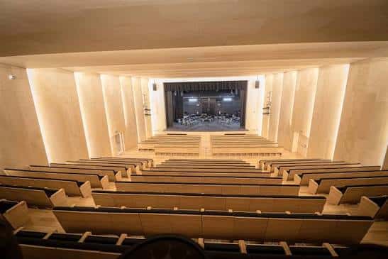 Vista panorámica del interior del auditorio vacío, mostrando las gradas de madera y el escenario iluminado