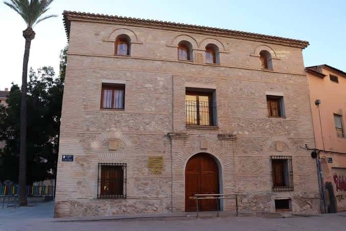Vista frontal de la Casa de las Cayitas, edificio histórico de piedra con fachada de tres plantas y puerta de madera