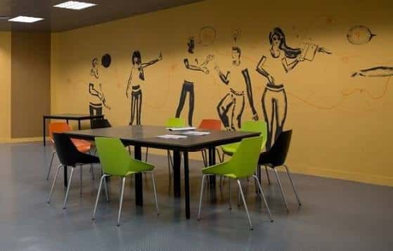 Sala interior con murales artísticos y mesas para actividades juveniles