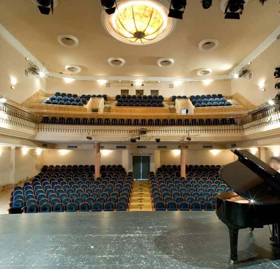 Interior del Teatro Gutiérrez de Alba con butacas azules y piano en el escenario