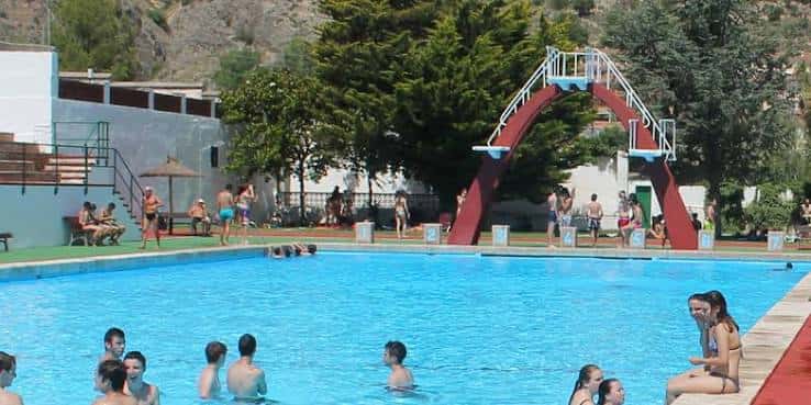 Vista de la piscina principal con gente nadando y el arco de saltos al fondo