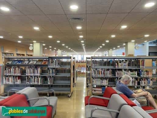 Interior de la biblioteca con estanterías, zona de lectura y usuarios
