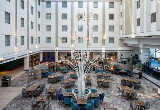 Vista panorámica del atrio principal del hotel con una gran escultura de árbol de luces y mesas de comedor
