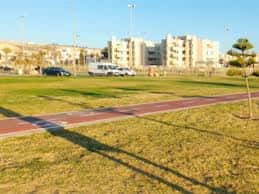 Vista panorámica del campo de rugby con sendero y edificios residenciales al fondo