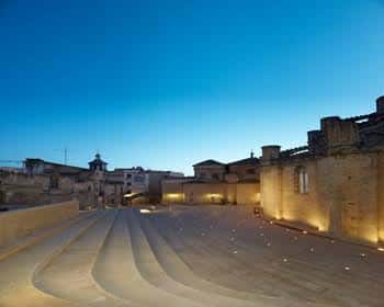 Vista nocturna de la Plaça de l'Absis con iluminación cálida y gradas curvas