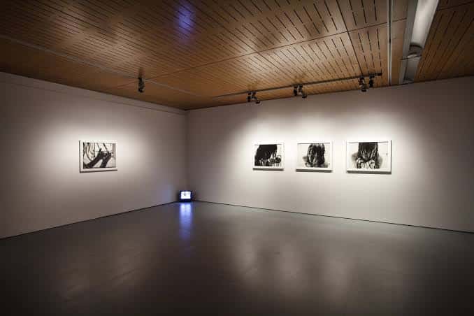 Sala de exposición con obras de arte enmarcadas y techo de madera