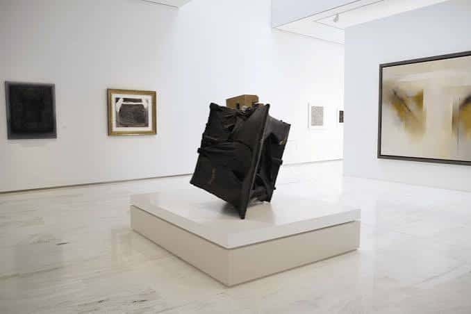 Exposición interior con escultura moderna en pedestal blanco