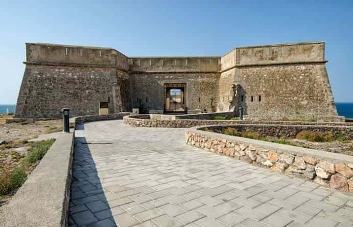 Vista frontal del Castillo de Guardias Viejas con camino de acceso pavimentado y mar al fondo