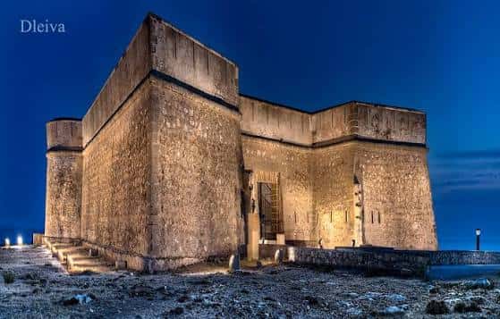 Castillo de Guardias Viejas iluminado por la noche con cielo azul oscuro y entorno costero