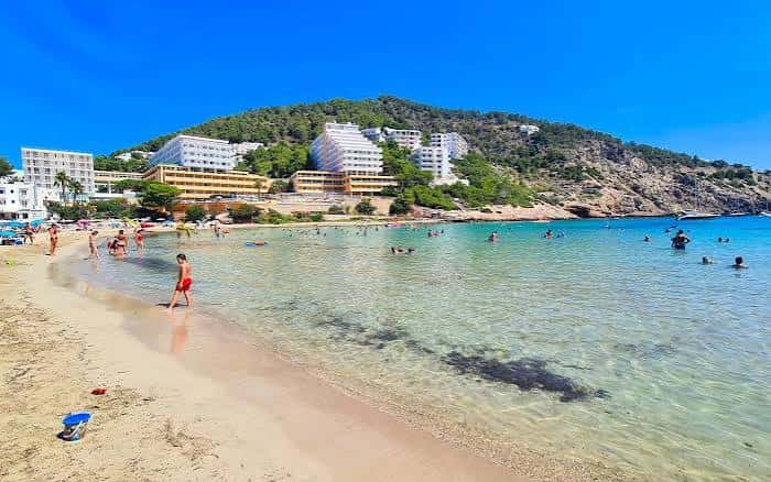 Playa de Cala Llonga con turistas disfrutando del agua cristalina y hoteles al fondo