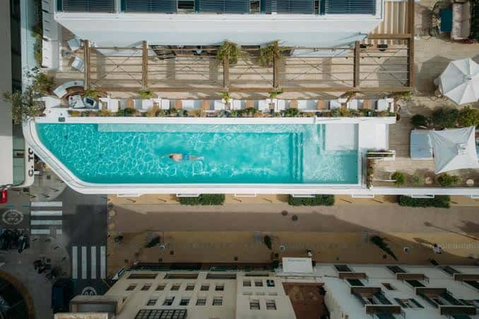 Perspectiva cenital de la piscina del hotel con una persona nadando y zonas de descanso