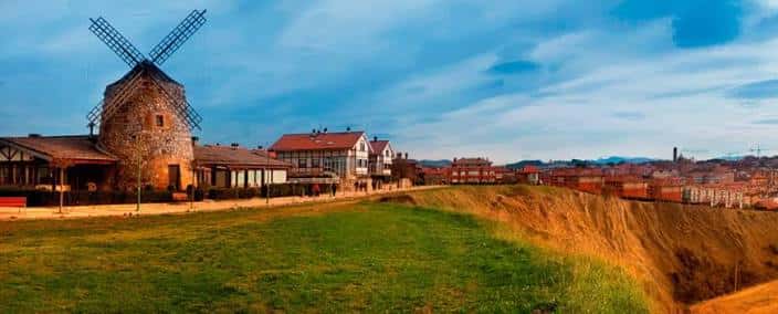 Vista panorámica de las campas de Aixerrota con el molino tradicional y edificios de Getxo al atardecer