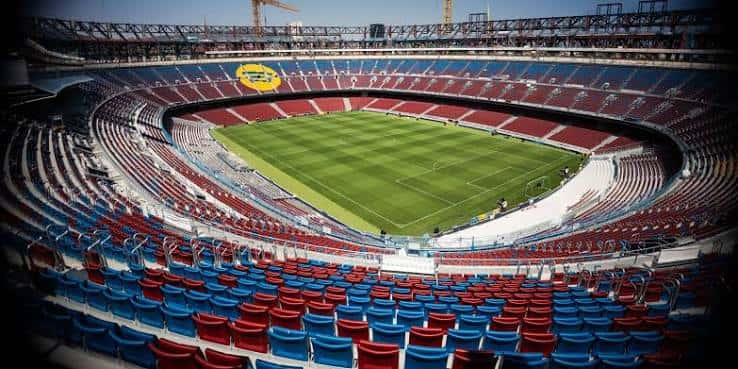 Vista panorámica del interior del estadio con gradas rojas y azules y campo de fútbol