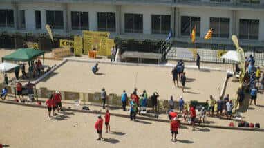 Vista aérea de un pisto municipal de petanca con jugadores en acción y público alrededor