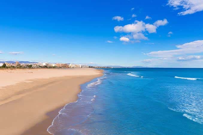Playa extensa con olas suaves y cielo azul despejado en el Puerto de Sagunto