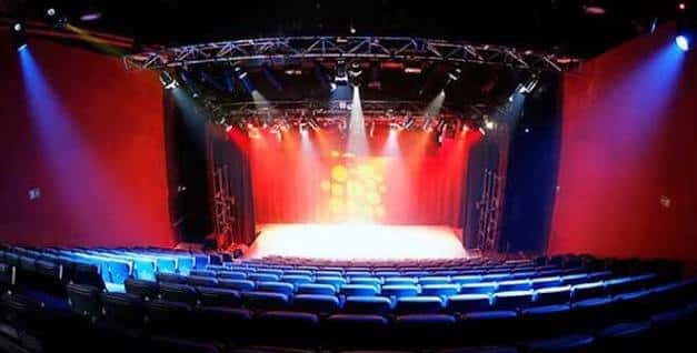 Vista interior del auditorio con escenario iluminado y butacas azules