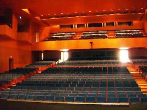 Vista general del auditorio con gradas y asientos azules bajo iluminación cálida