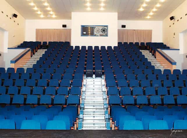 Interior del auditorio con butacas azules y escalera central de acceso