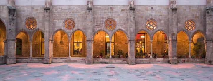 Fachada iluminada del convento al atardecer, mostrando los arcos y ventanas decoradas