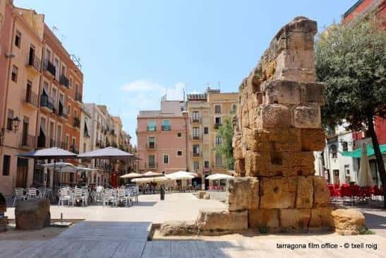 Plaza del Fòrum con mesas de restaurante y ruinas romanas bajo el sol