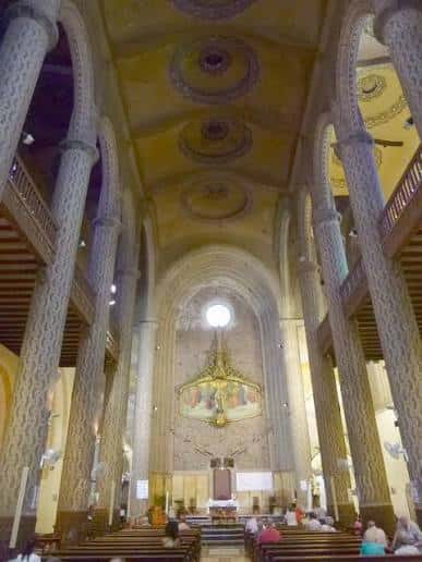 Interior de la iglesia con columnas ornamentadas, bóveda decorada y altar principal bajo luz natural