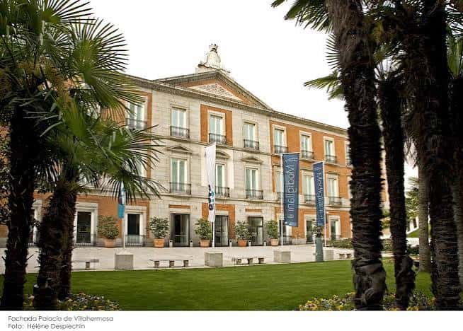 Fachada principal del Palacio de Villahermosa enmarcada por palmeras, con banderas del museo y jardín delantero