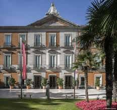 Vista frontal del Palacio de Villahermosa con palmeras y flores en primer plano, bajo cielo despejado