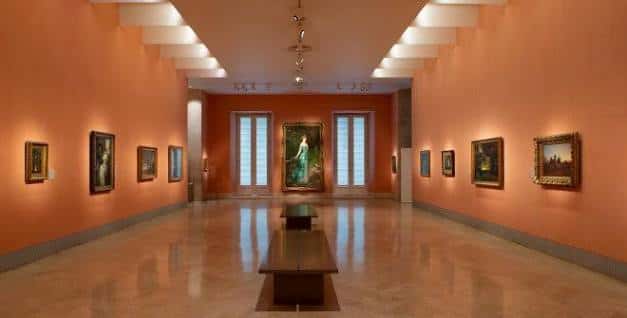 Galería interior del Museo Thyssen-Bornemisza con paredes color salmón, cuadros enmarcados y bancos de madera