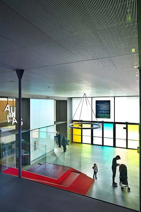 Hall principal con escalera roja, iluminación moderna y personas transitando por el espacio