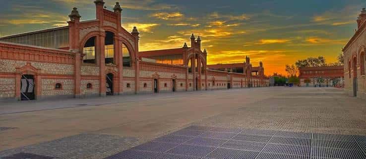 Vista panorámica del Matadero Madrid al atardecer con fachada de ladrillo y cielo dorado