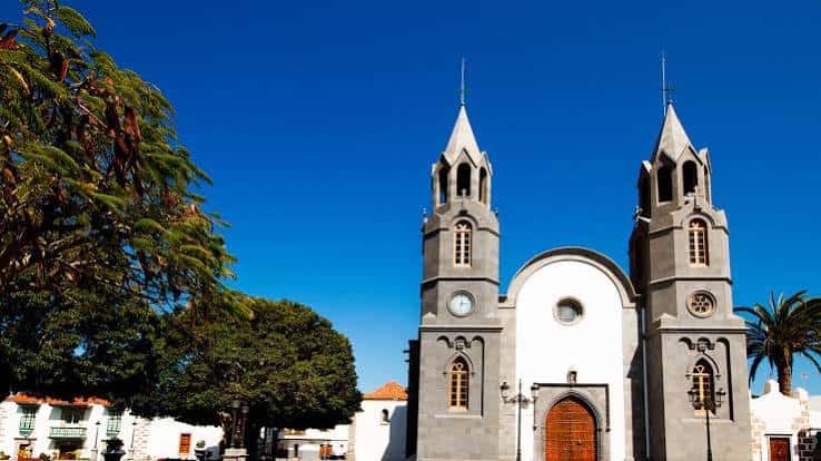 Fachada de la Iglesia de San Juan Bautista con sus dos torres gemelas bajo un cielo azul