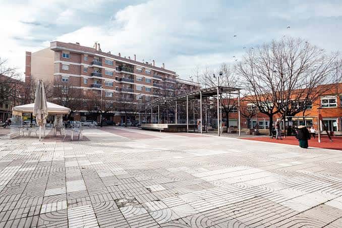 Plaza vacía con pavimento decorativo, árboles sin hojas y estructura metálica