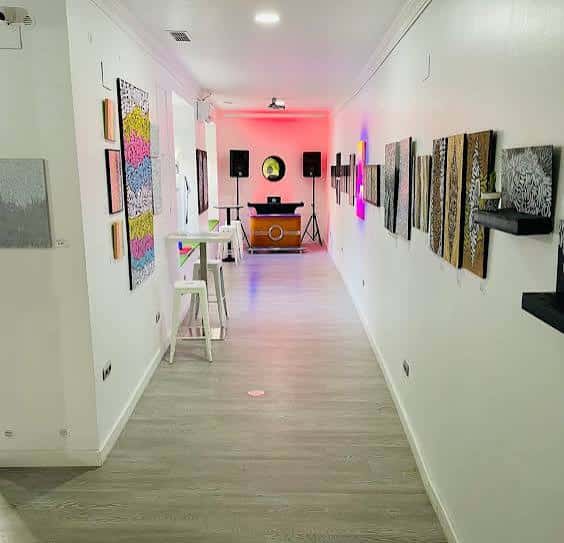 Interior del espacio con galería de arte, iluminación de colores y zona de DJ