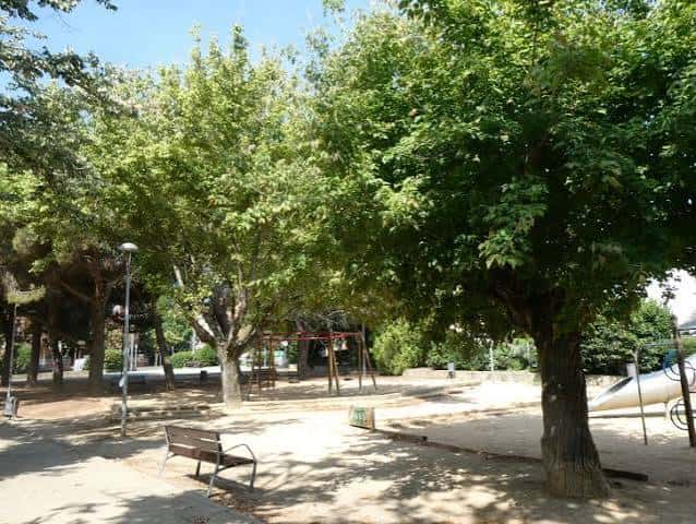 Área arbolada del parque con bancos y zona de juegos al fondo