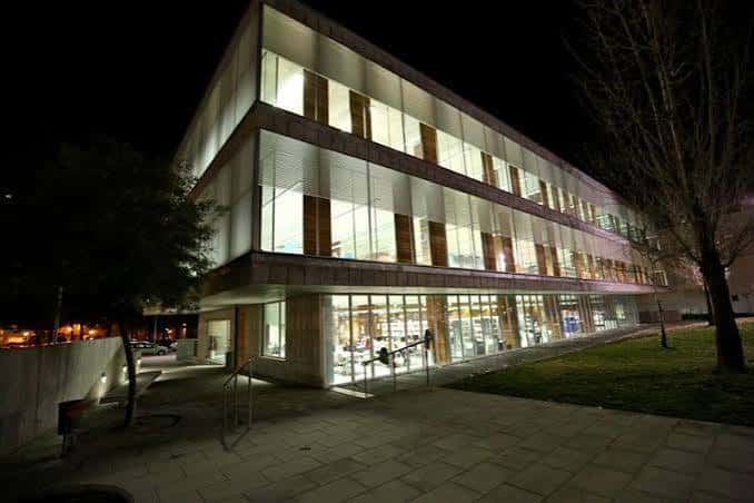 Vista nocturna de la biblioteca iluminada, mostrando su arquitectura contemporánea y accesibilidad