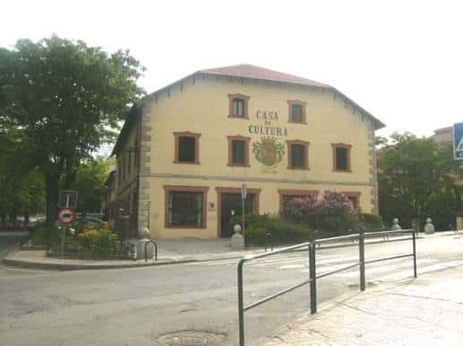 Vista exterior diurna de la Casa de la Cultura de Collado Villalba con fachada amarilla y escudo municipal