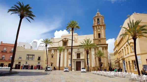 Vista frontal de la Catedral de Cádiz con palmeras y sillas blancas dispuestas en la plaza