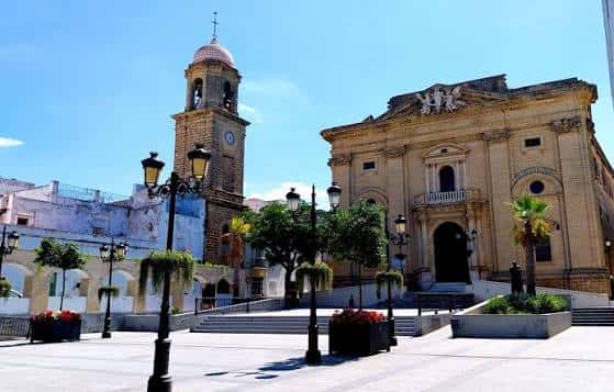 Vista diurna de la Plaza Mayor con la Iglesia de San Juan Bautista y su torre campanario bajo un cielo azul