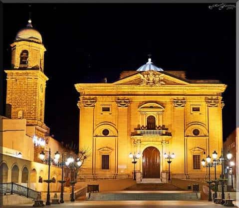 Iglesia de San Juan Bautista en la Plaza Mayor durante la noche, con iluminación cálida que resalta su arquitectura