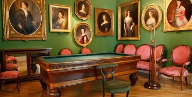 Sala de billar con paredes verdes y retratos de época